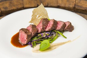 A plate of sliced steak with vegetables and a sauce. - Greenside (De Koog)