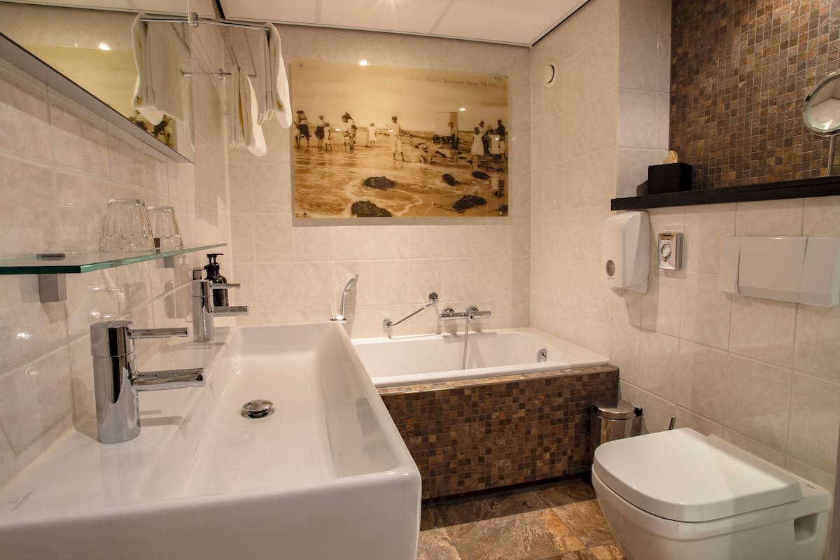 A modern bathroom with a large bathtub, a separate toilet, and a glass shelf with toiletries.