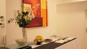 A room with a vase of flowers, a fruit bowl, a painting, and a table with a placemat. - Pension A Und A (Vienna)