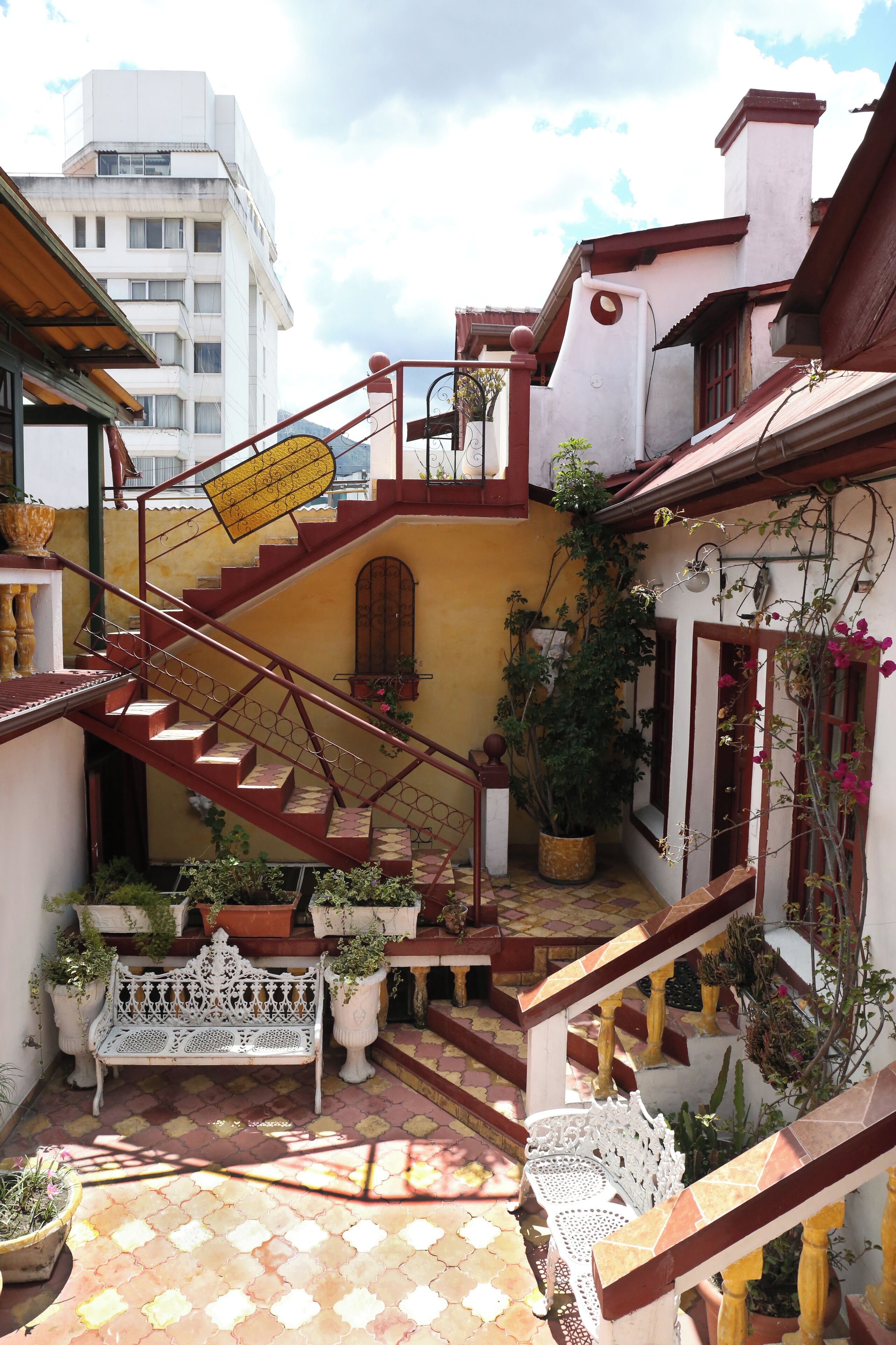 A courtyard with a central staircase, potted plants, and a white bench.