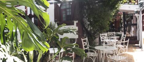 Un patio con sillas y mesas de metal blanco, rodeado de exuberante vegetación y un suelo con diseño.