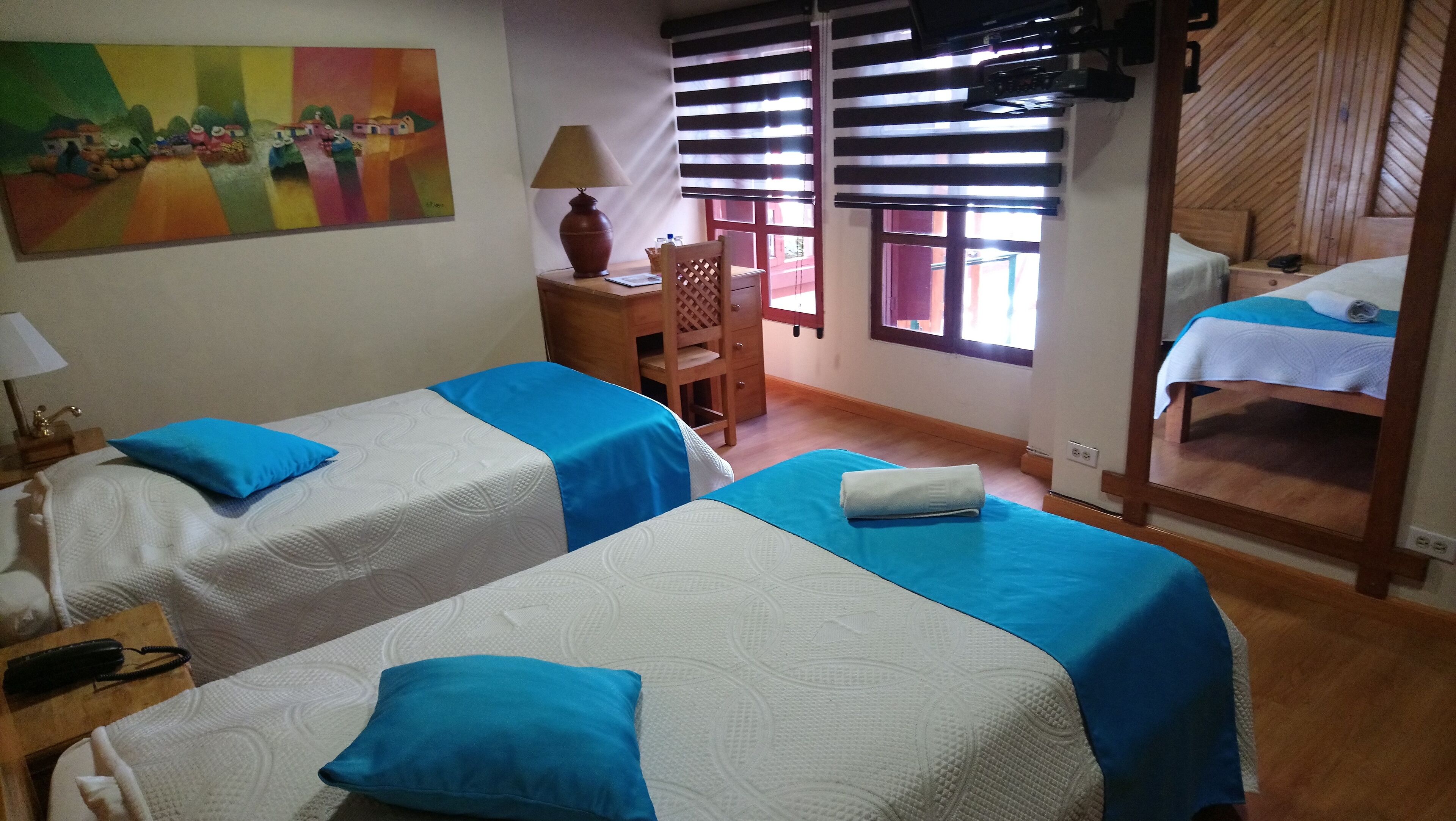 Habitación de hotel con dos camas, un escritorio, una silla, una lámpara y un cuadro en la pared.