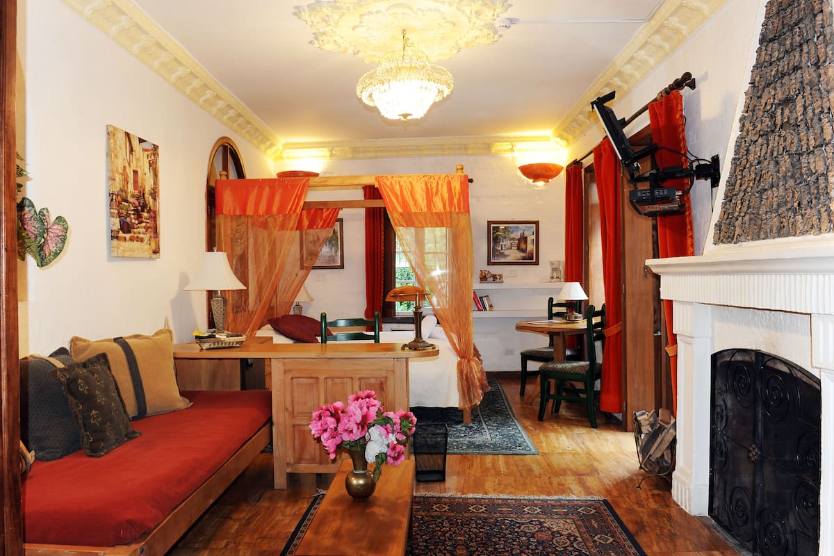 A cozy living room with a sofa, a table with a vase of flowers, a fireplace, and a dining area with chairs and a table.