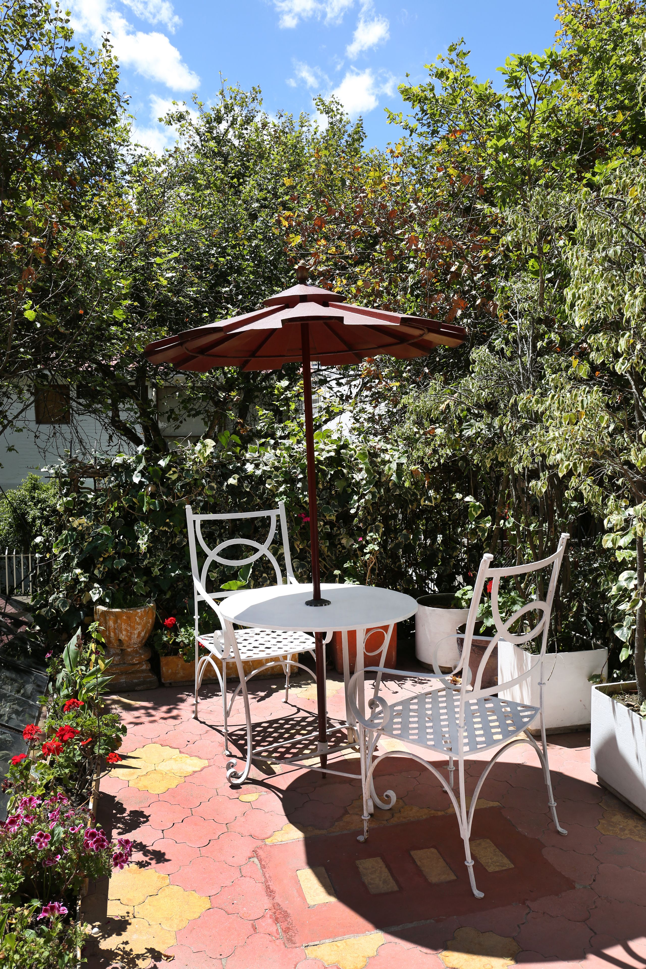 A patio with a table and chairs, surrounded by potted plants and a red umbrella.