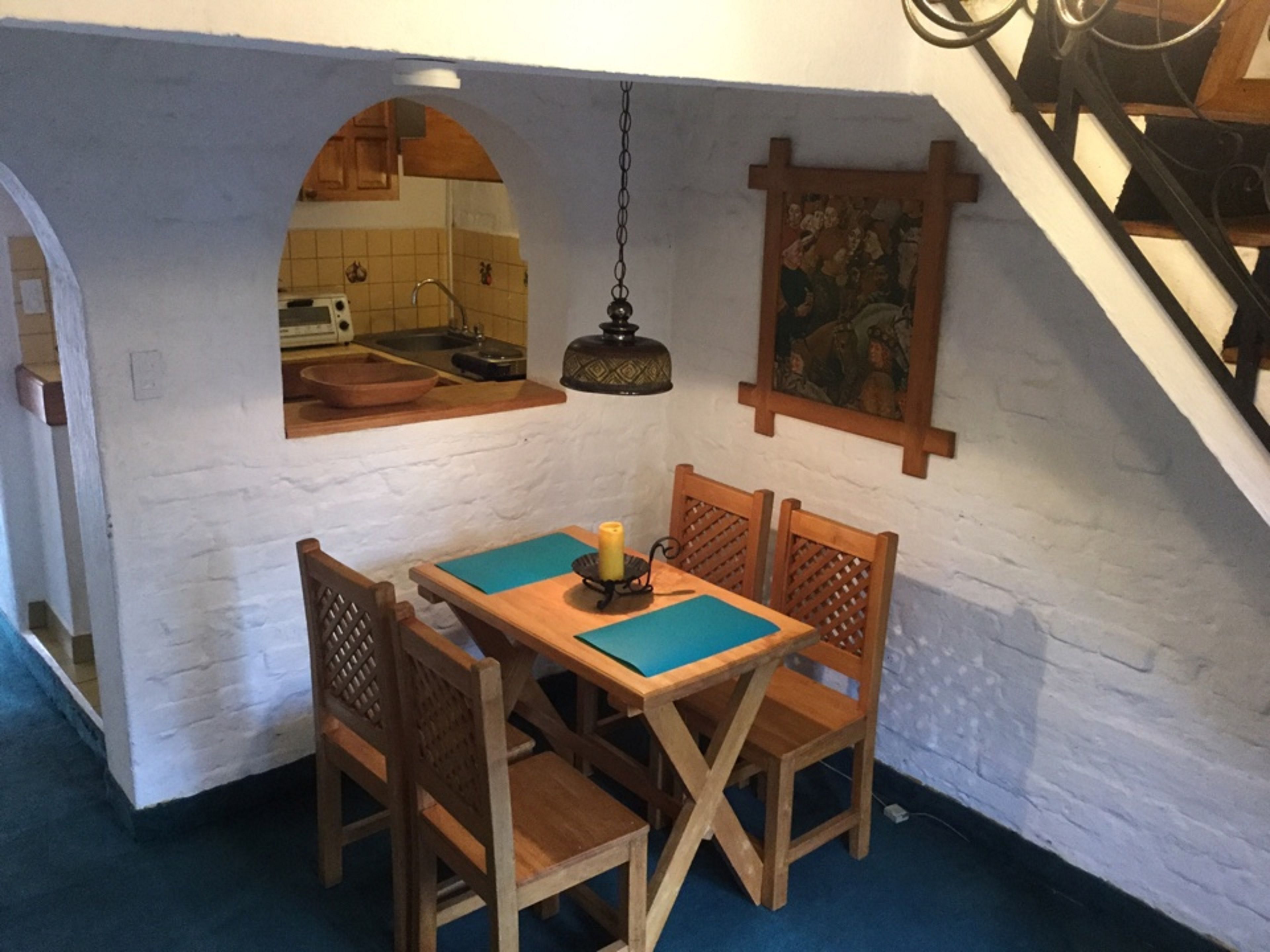 A dining area with a table and chairs, a hanging light fixture, and a kitchen visible through an archway.