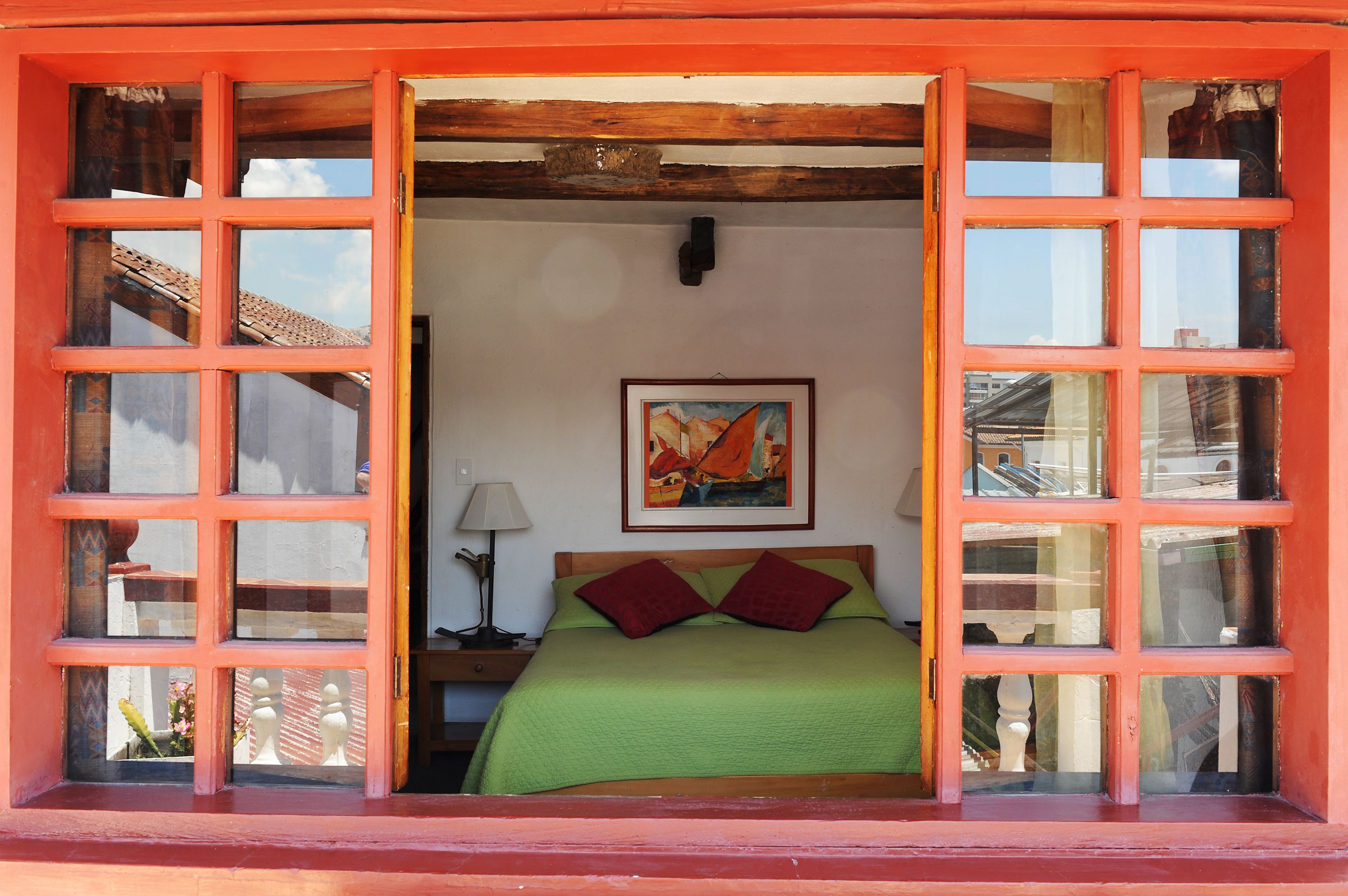 Una stanza con un letto, un quadro appeso al muro e una finestra vista esterna.