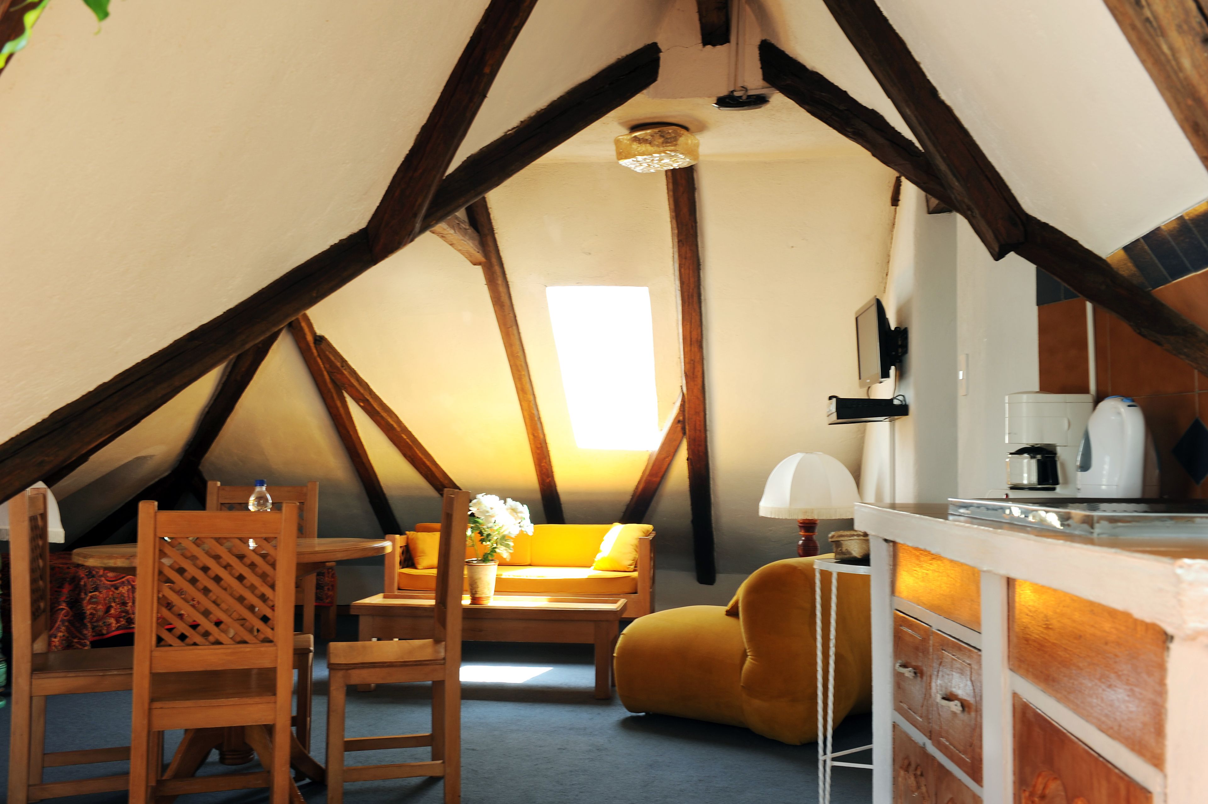 Ein gemütliches Dachzimmer mit Holzbalkendecke, einer Couch, einem Sessel, einem kleinen Tisch und einem Schrank.
