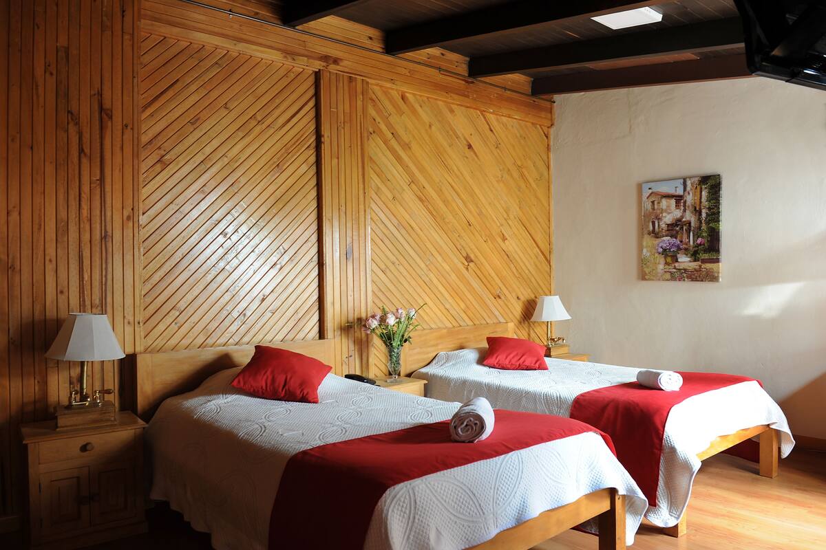 A room with two beds, wooden paneling, a painting on the wall, and a nightstand with a lamp.