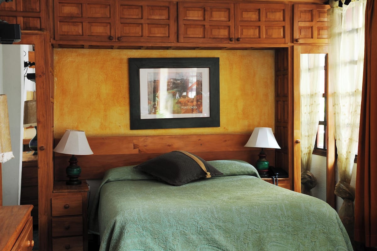 A bedroom with a wooden headboard, two bedside tables with lamps, a green bedspread, and a framed picture on the wall.