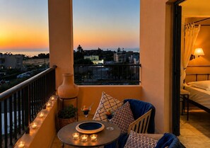 Un balcon donnant sur un coucher de soleil, une table éclairée à la bougie et un vase.