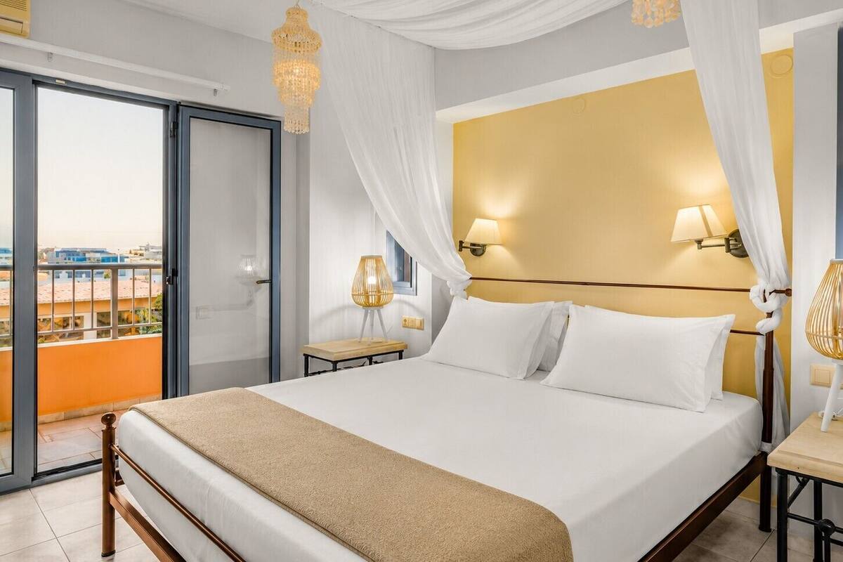 A hotel room with a bed, a nightstand, a lamp, and a view of buildings through a glass door.