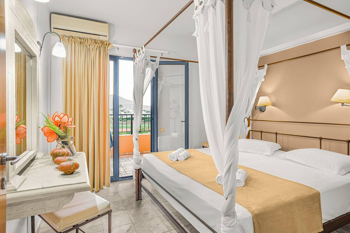 A hotel room with a bed, a bedside table, a mirror, a window with curtains, and a view of the outdoors.
