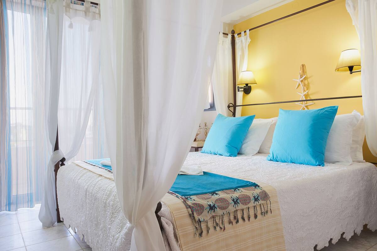 A bedroom with a bed, white curtains, a yellow wall, and two bedside lamps.