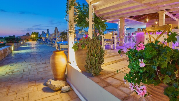 A terrace with a stone pathway, potted plants, and outdoor seating under a wooden pergola. - Golden Bay Apartments-Garden Haven (Hersonissos)