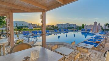 Un área al lado de la piscina con sillones de descanso, sombrillas y vistas a la piscina y edificios a lo lejos.