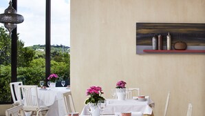 A dining area with tables set for four, white chairs, and a view of greenery through large windows. - Parque Das Laranjeiras (Loulé)