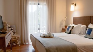 A hotel room with a bed, a desk, a chair, a window with curtains, a bedside lamp, and a small potted plant. - Parque Das Laranjeiras (Loulé)