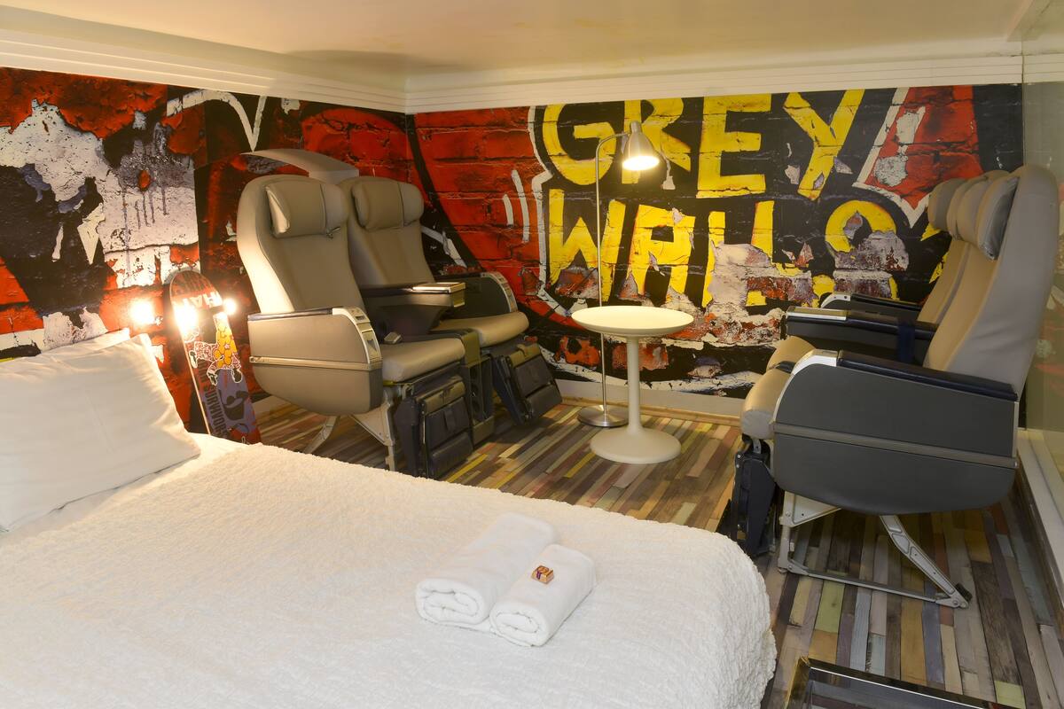 A hotel room with a bed, two armchairs, a small round table, and a wall with graffiti art.