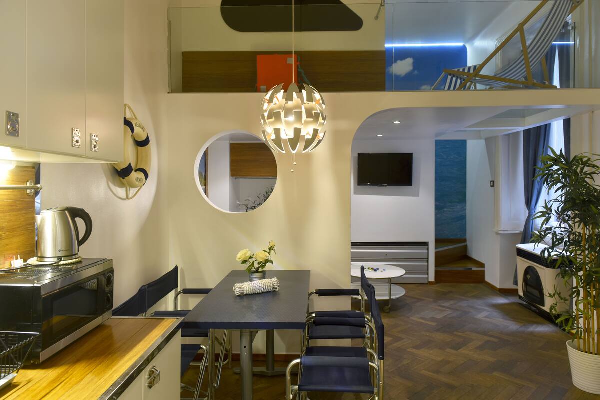 A modern kitchen with a dining area, a kettle, a microwave, and a potted plant.