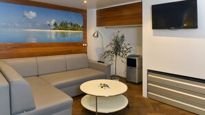 En moderne stue med sofa, sofabord, fjernsyn og et maleri af en strand.