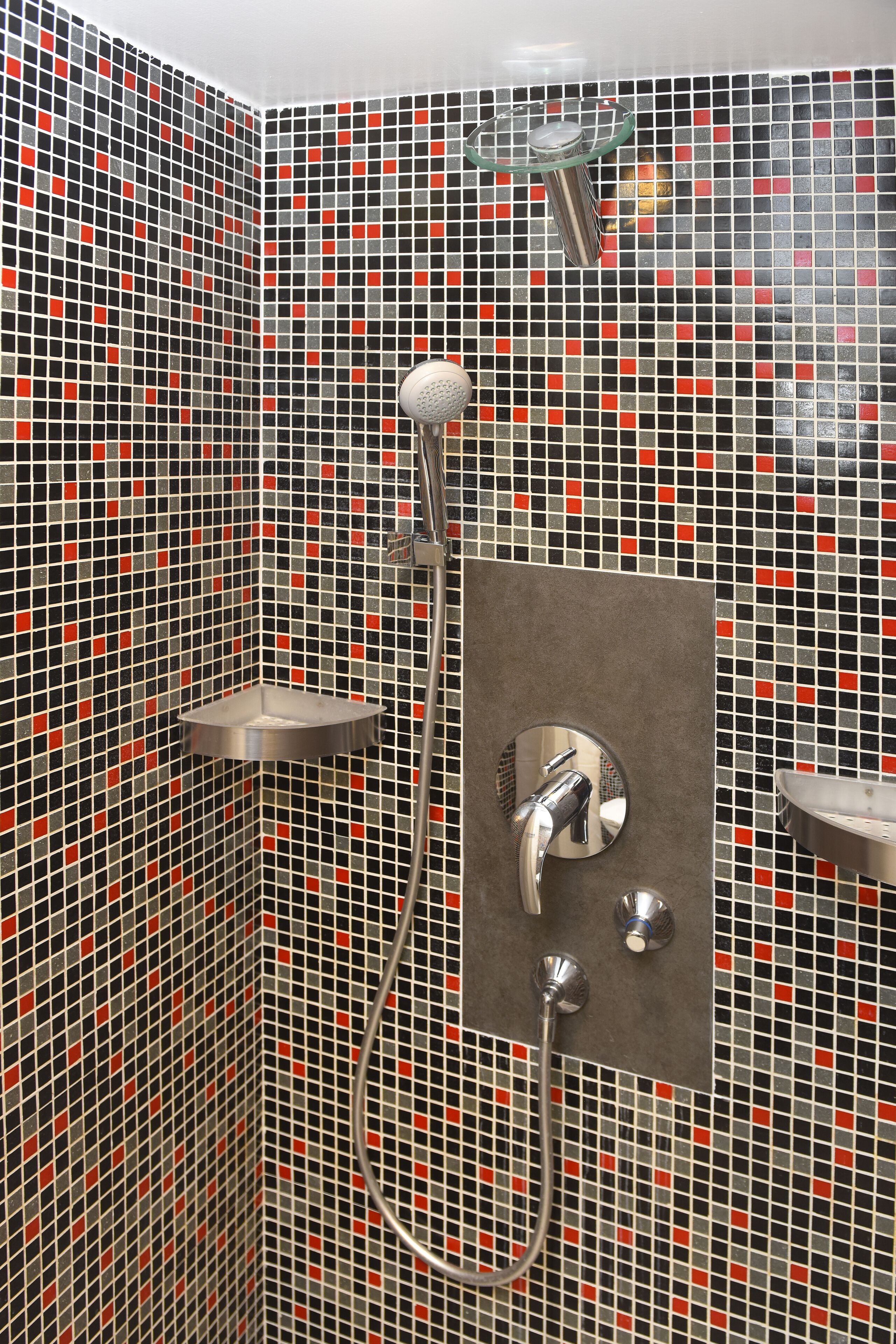 Un área de ducha con pared de azulejos, un cabezal de ducha de mano y un grifo instalado en la pared.