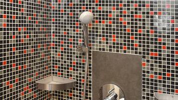 Un área de ducha con pared de azulejos, un cabezal de ducha de mano y un grifo instalado en la pared.