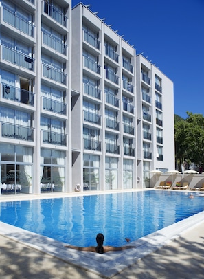 A modern hotel with a swimming pool, multiple balconies, and sun loungers. - Tara Hotel (Becici)