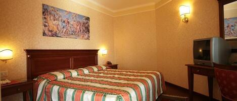 A hotel room with a large bed, a desk with a television, and a painting on the wall.