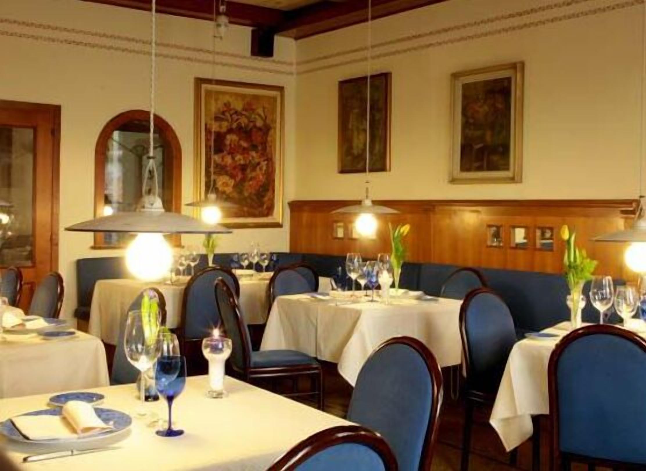 Un restaurant où les tables sont dressées pour le service, avec des chaises à l’assise bleue et des nappes blanches.
