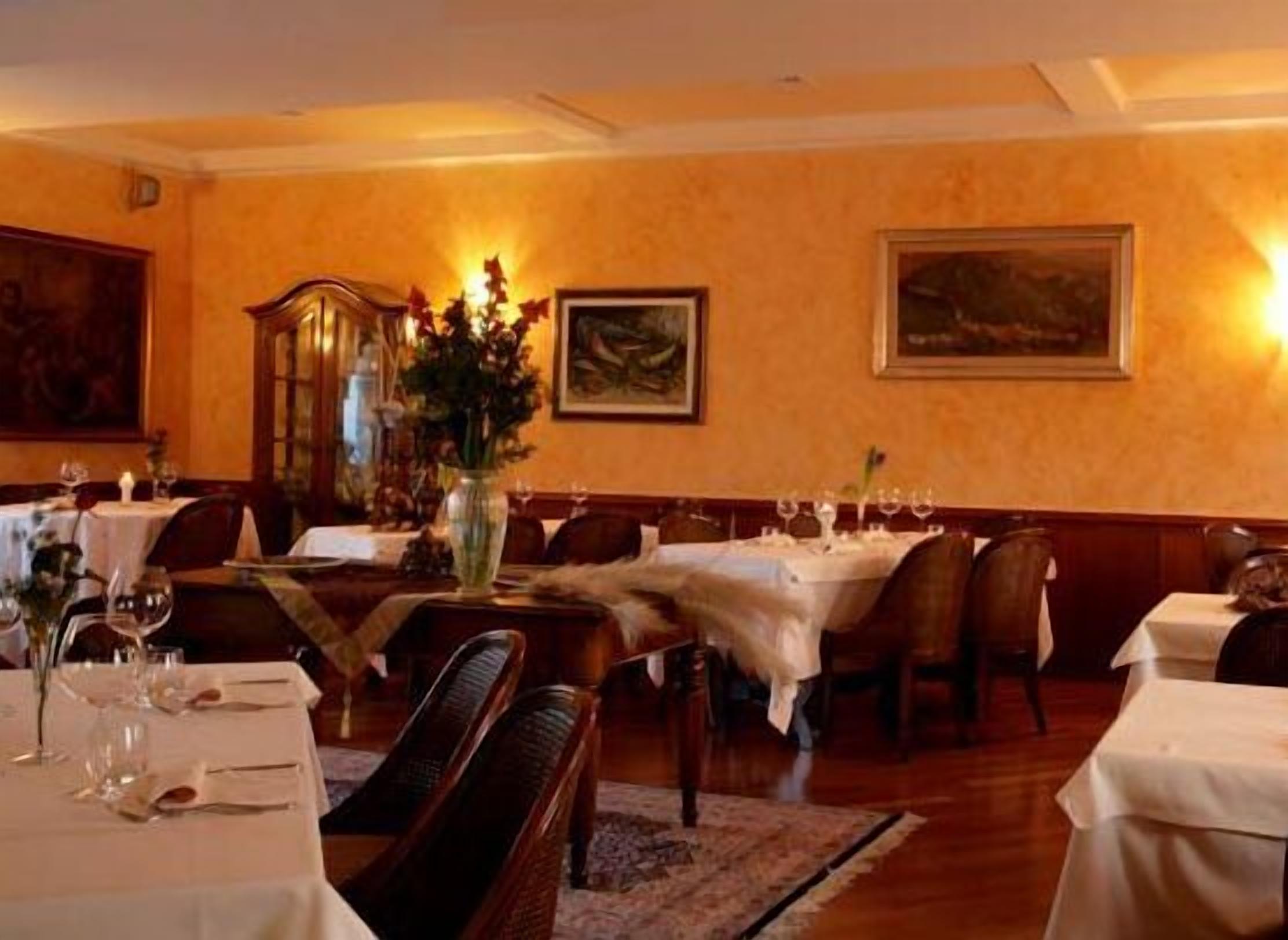 A dining area with tables set for two, each with a vase of flowers and wine glasses.