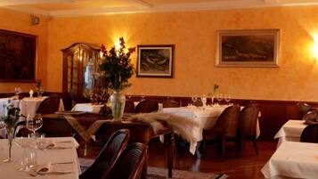 A dining area with tables set for two, each with a vase of flowers and wine glasses.