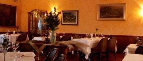 A dining area with tables set for two, each with a vase of flowers and wine glasses.