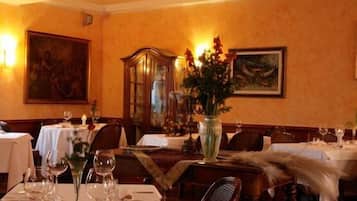 A dining room with tables set for a meal, featuring a vase with flowers and a painting on the wall.