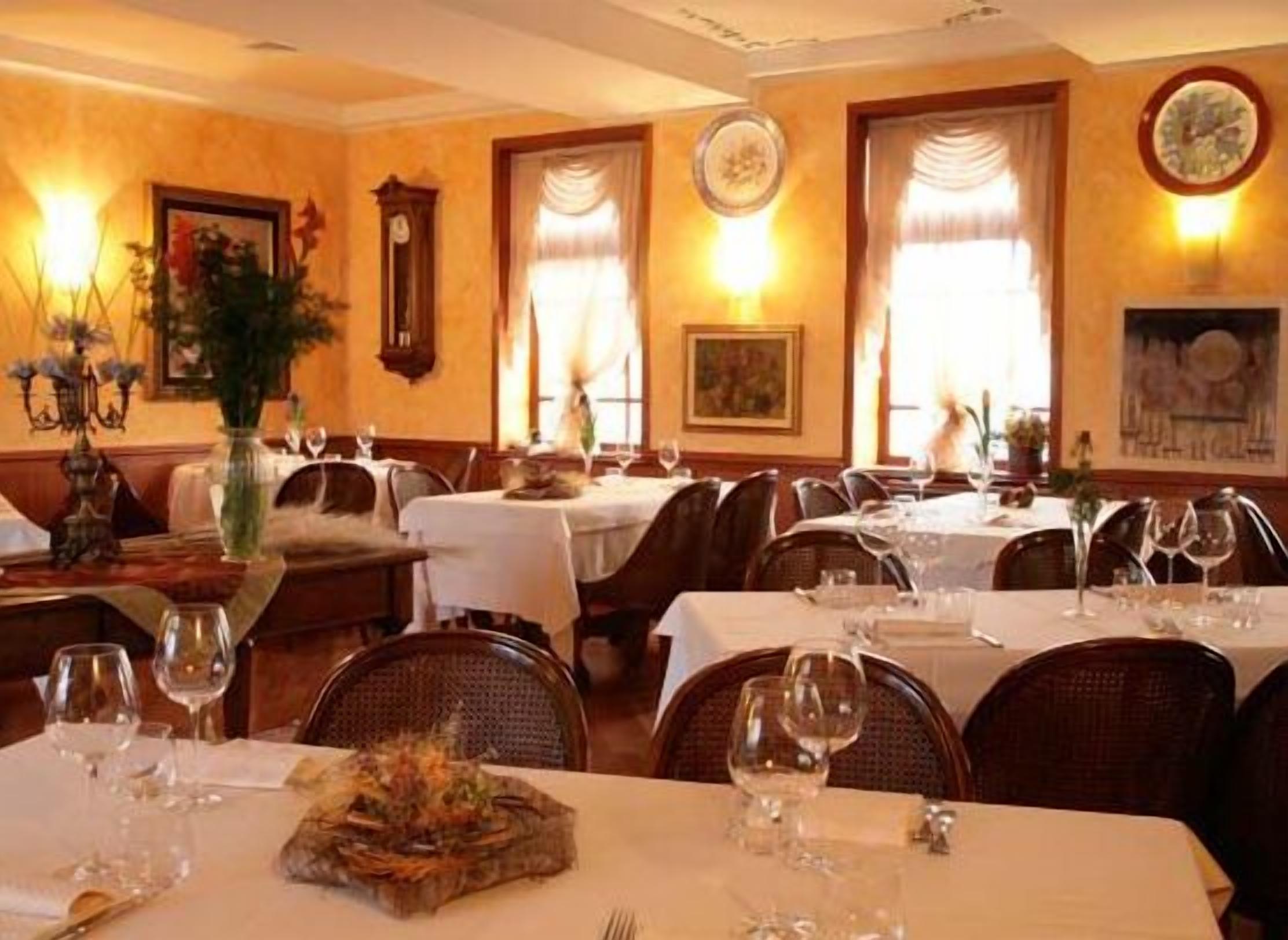 Un restaurante con varias mesas, cada una dispuesta con copas de vino y cubiertos, y un centro de mesa en una de ellas.