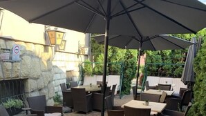 An outdoor patio with wicker furniture, a stone wall, and a large umbrella providing shade. - Hunyadi (Gyor)
