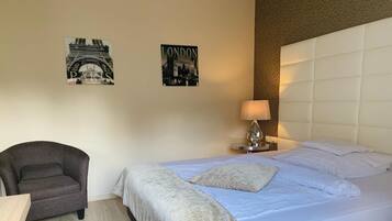 Habitación de hotel con cama, una silla, mesita de noche con lámpara y dos obras de arte murales que representan París y Londres.