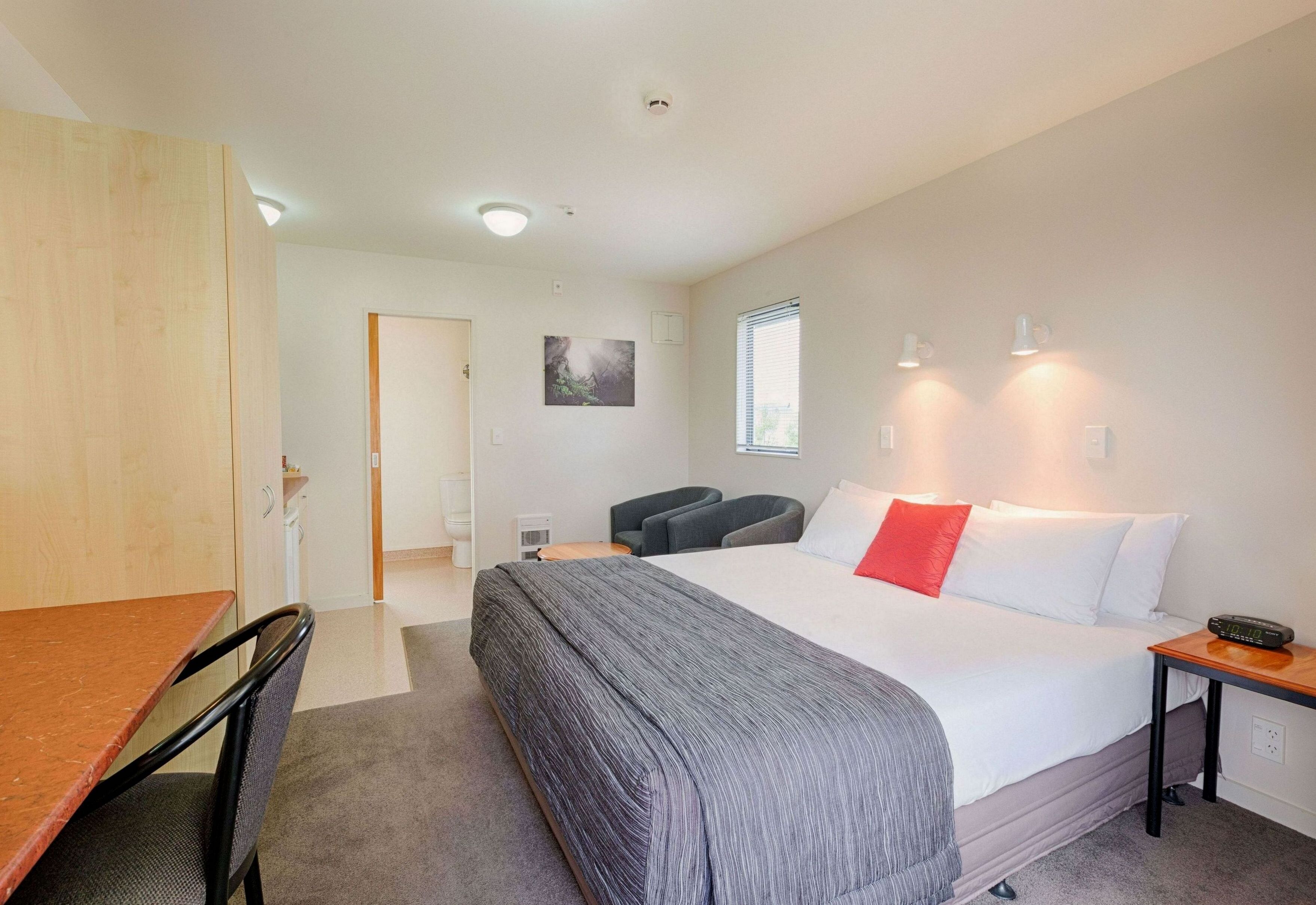 Een hotelkamer met een bed, een bureau, een stoel, een tafeltje, een raam en een deur.