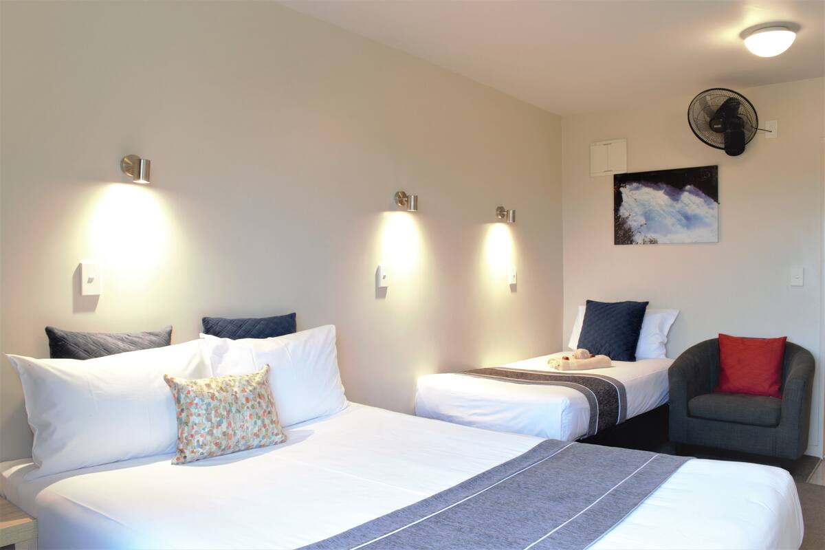 A hotel room with two beds, a chair, and a ceiling fan.
