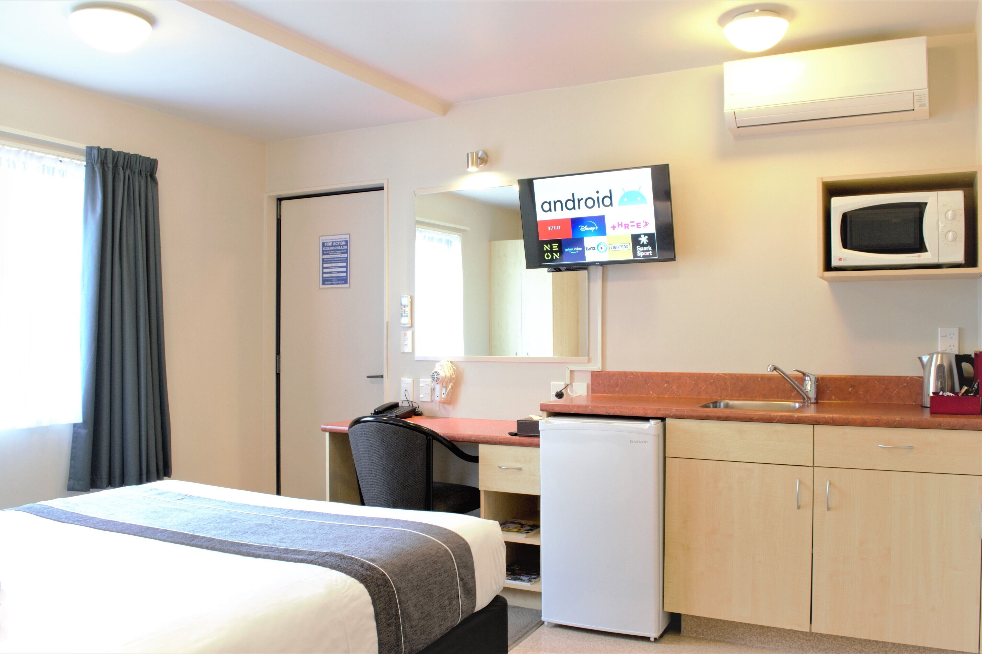 Une chambre d’hôtel équipée d’un lit, d’un bureau, d’une chaise, d’un four à micro-ondes et d’un téléviseur affichant une interface Android.