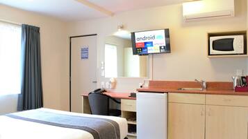 Une chambre d’hôtel équipée d’un lit, d’un bureau, d’une chaise, d’un four à micro-ondes et d’un téléviseur affichant une interface Android.