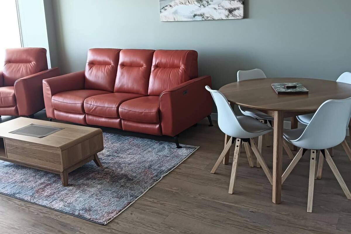A modern living room with a red leather sofa, a wooden coffee table, and a dining table with white chairs.