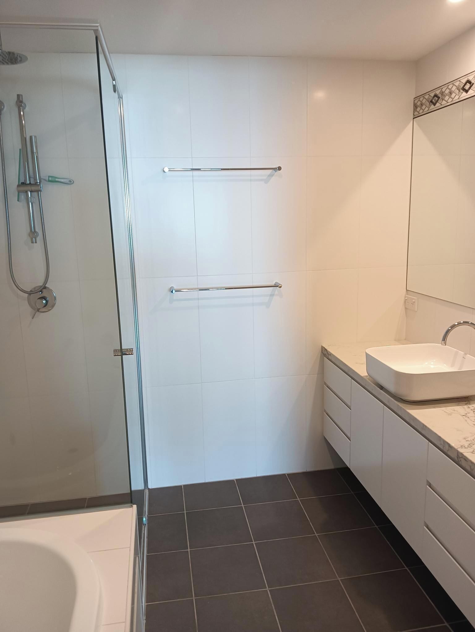 Une salle de bain moderne avec une douche à l’italienne en verre, un lavabo blanc et un grand miroir.
