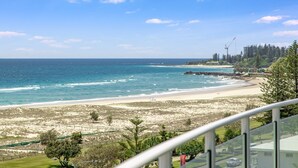 A coastal view with a sandy beach, ocean, and a forested area with buildings in the background. - Kirra Surf Apartments (Coolangatta)