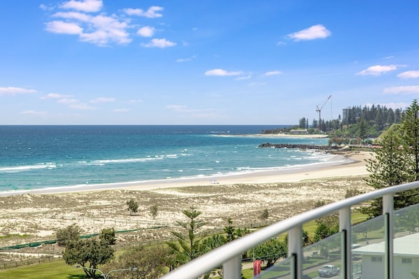 A coastal view with a sandy beach, ocean, and a forested area with buildings in the background. - Kirra Surf Apartments (Coolangatta)