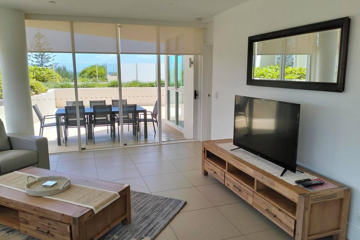 A modern living room with a TV, wooden furniture, a sofa, and a dining area with chairs and a table.