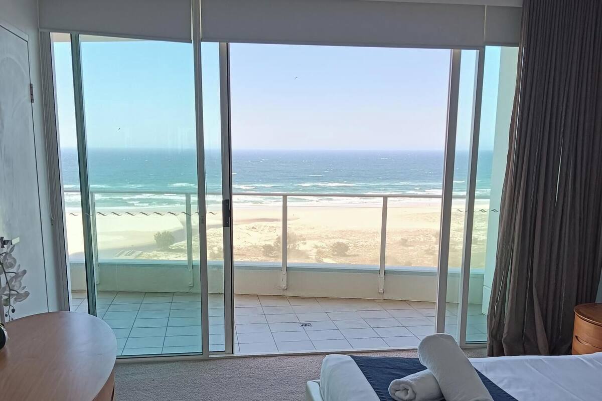 A hotel room with a large sliding glass door leading to a beach view.