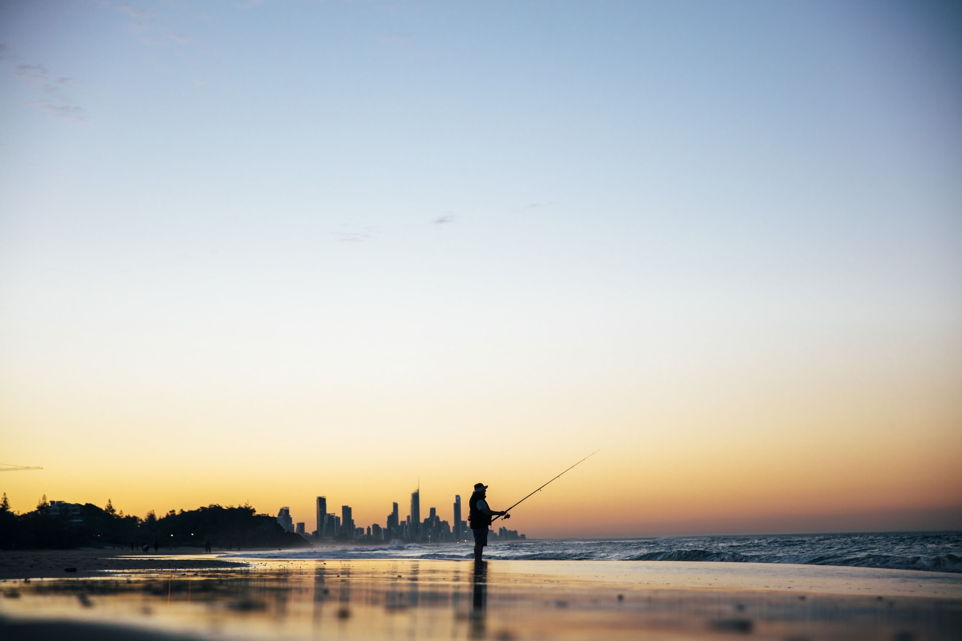 A person fishing on a beach with a city skyline in the background.