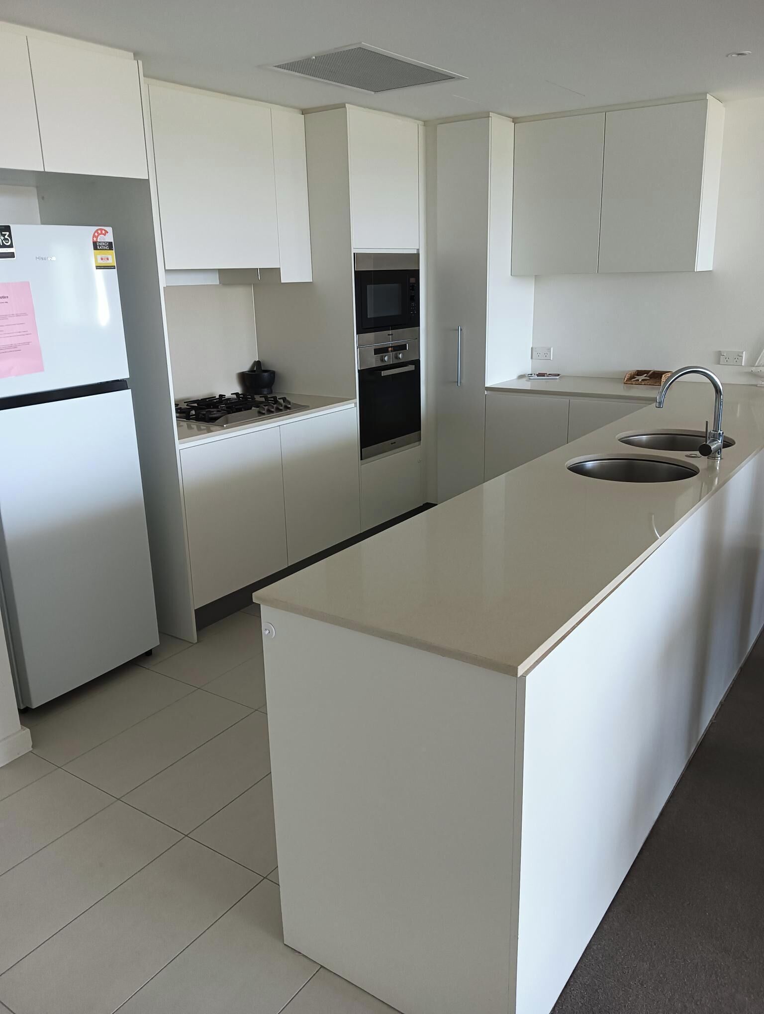 A modern kitchen with white cabinetry, a stainless steel refrigerator, a built-in oven, and a sink.