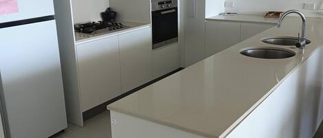 A modern kitchen with white cabinetry, a stainless steel refrigerator, a built-in oven, and a sink.