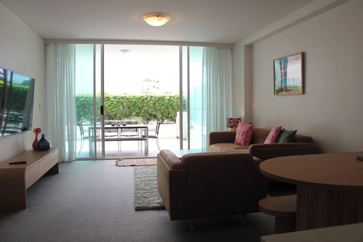 A modern living room with a sofa, a coffee table, a TV, and a sliding glass door leading to an outdoor area.